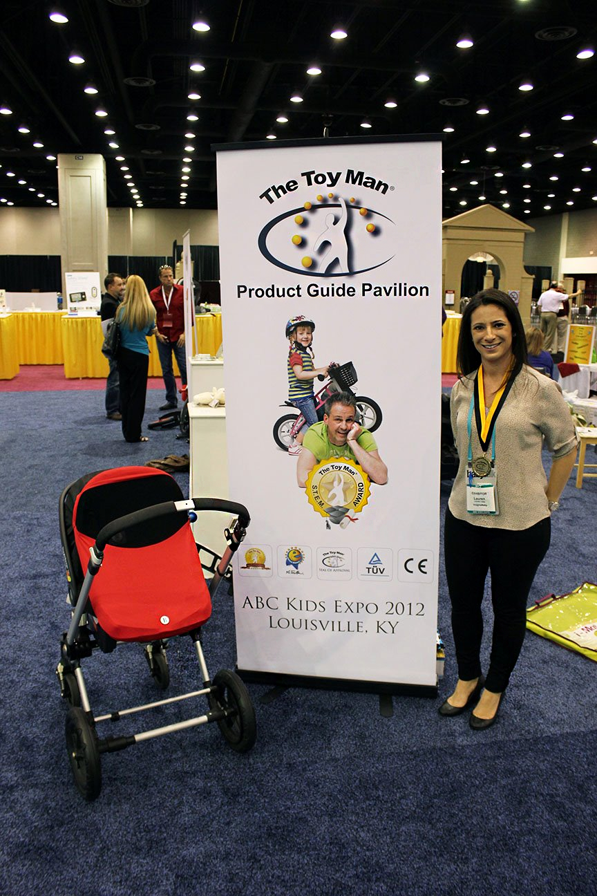 An exhibitor at ABC Expo 2012 posing for a photo next to the vertical banner at The Toy Man® Pavillion.